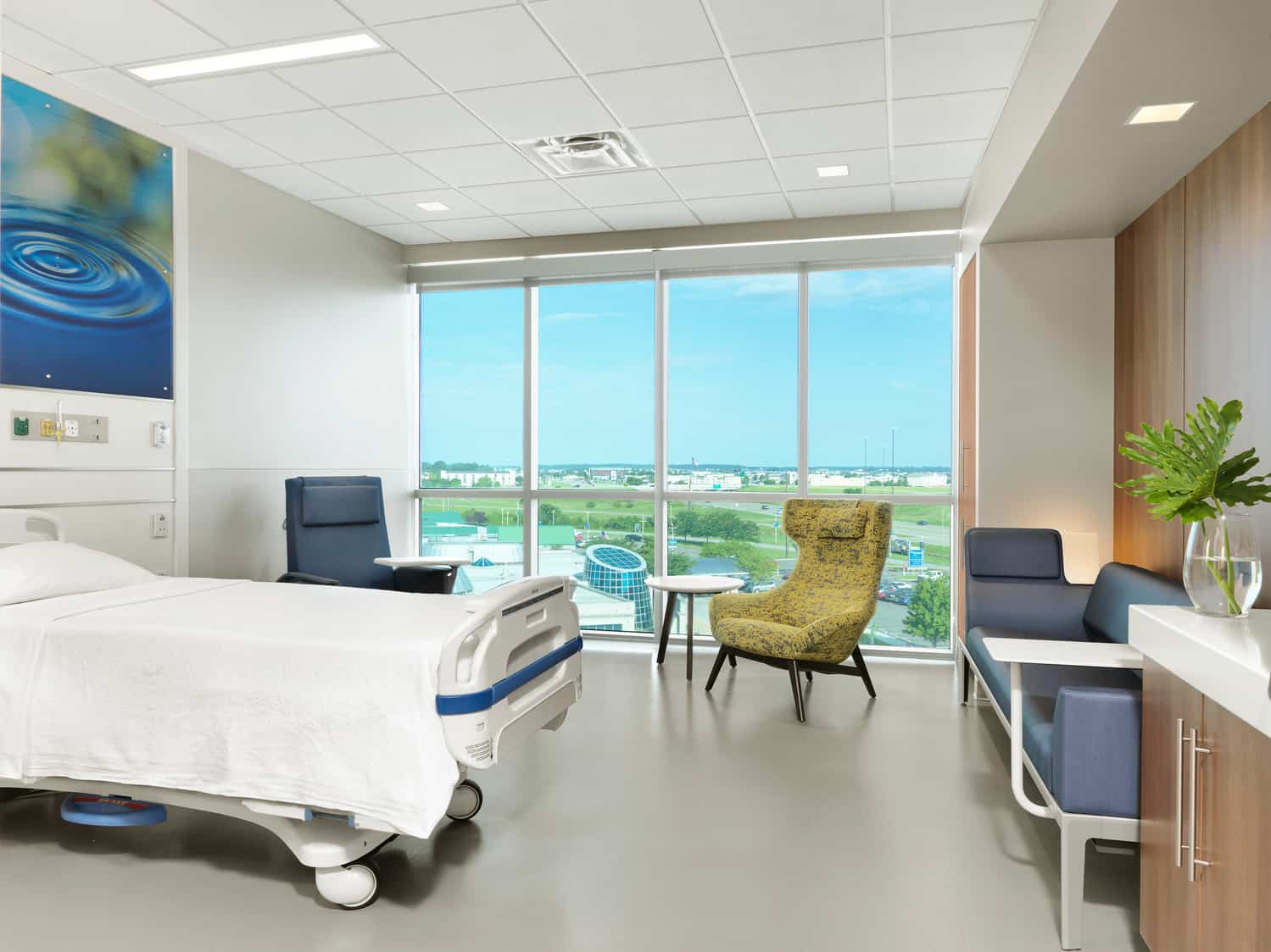 View of a private patient room within the Deaconess Hospital for overnight stays. The standard hospital bed is surrounded by a couch and two chairs for family members, and floor-to-ceiling windows allow for natural light to flood the room. The room is clean and attractive.