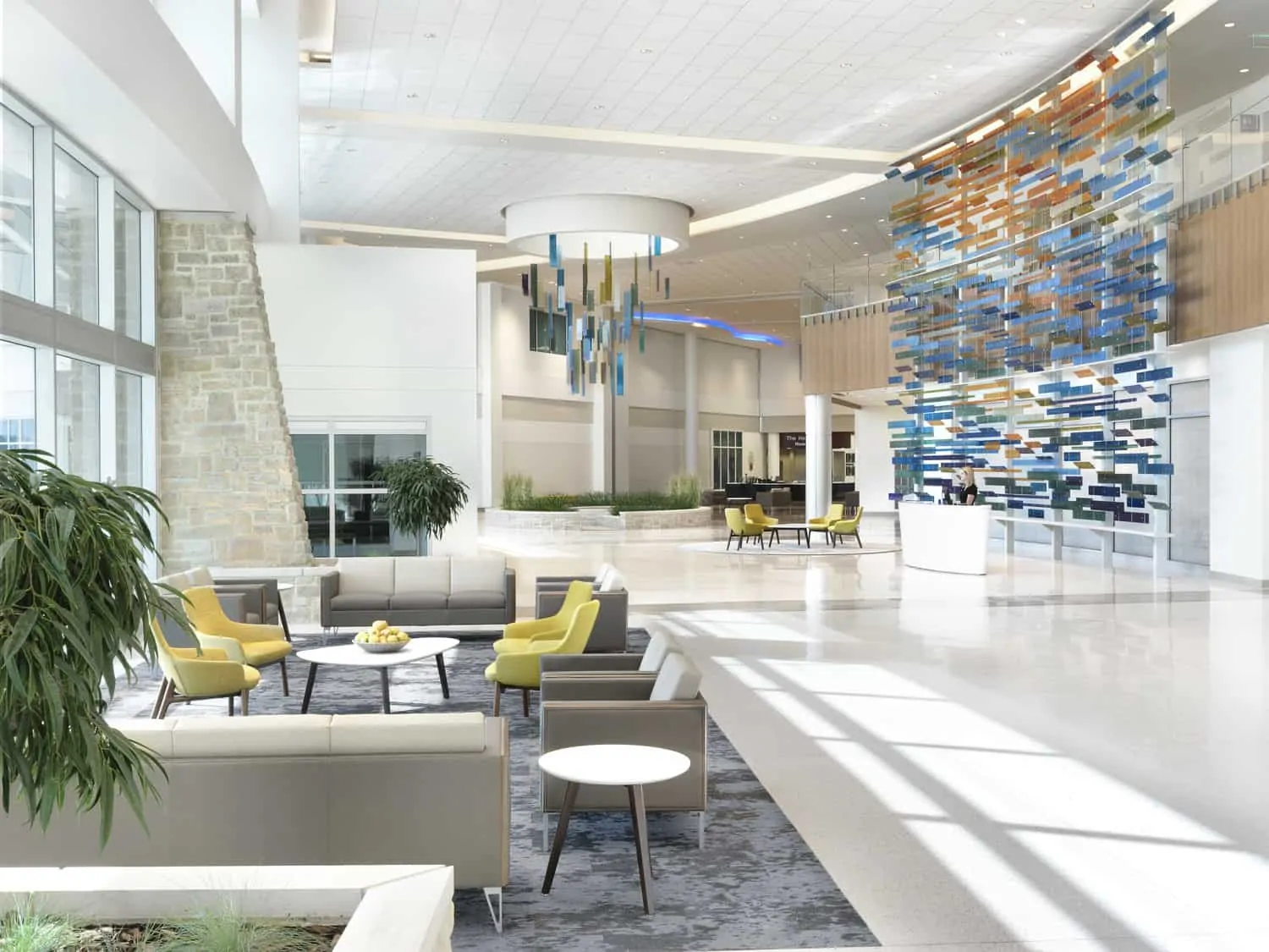 Natural light floods the space through a two story glass curtainwall and a skylight rotunda. The atmosphere is complete with modern interiors and comfortable waiting areas with modern green and grey furniture. A custom 20’ x 30’ hanging art feature inspired by the Ohio River sets the tone for a nature-centric healing environment. Glass panels in shades of green, blue, orange, teal, and brown are suspended, creating the illusion of waves. Additionally, a second hanging art installation is suspended over an interior stone garden, symbolizing movement and transformation. This image shows BSA's expertise in interior design.