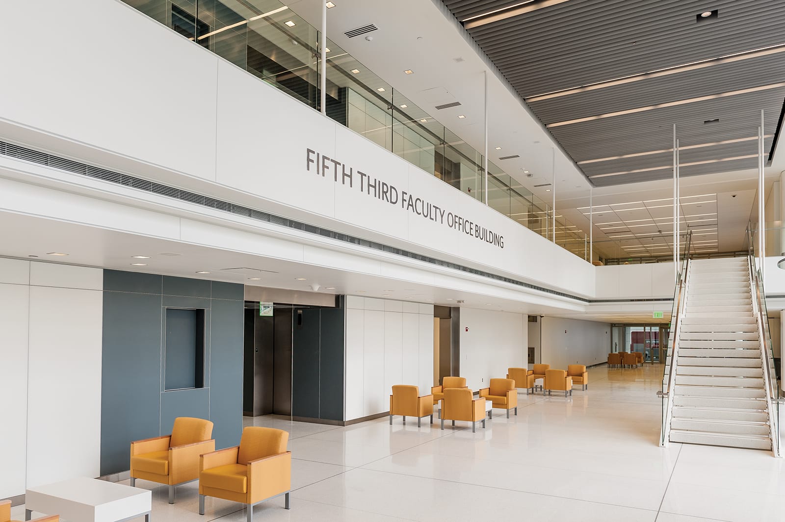 This image shows the interior lobby of the Fifth Third Faculty Office Building. The space features a modern, minimalist design with clean white walls and floors. Prominently displayed on the wall is the text 