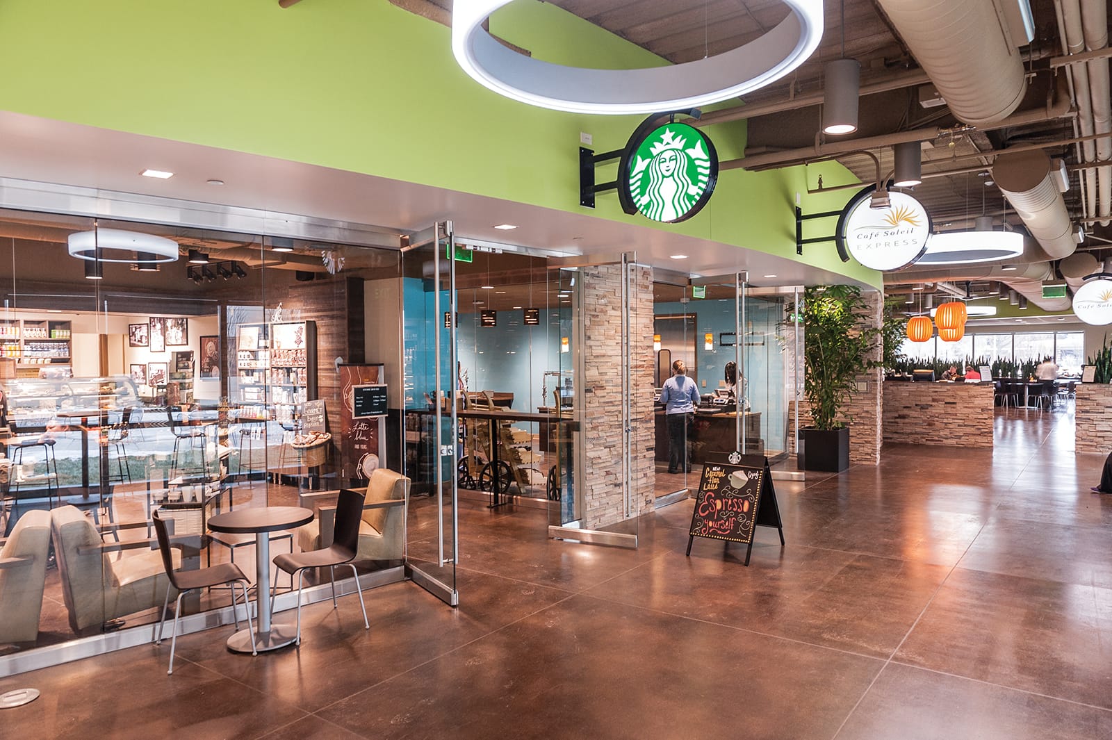 The image shows a modern café area inside the Fifth Third Faculty Office at Eskenazi Health, featuring a Starbucks café with its distinctive green logo sign mounted on a lime green wall, alongside another café called 