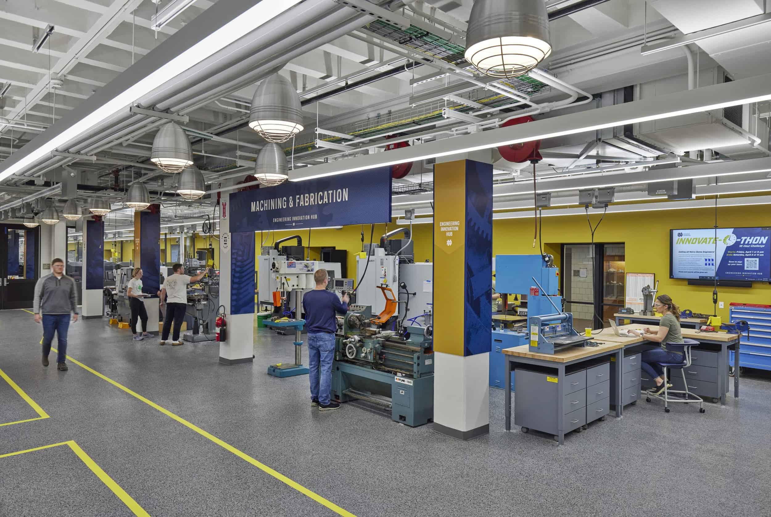 This image shows an advanced manufacturing and engineering innovation hub at Notre Dame. The space features deep blue walls with 