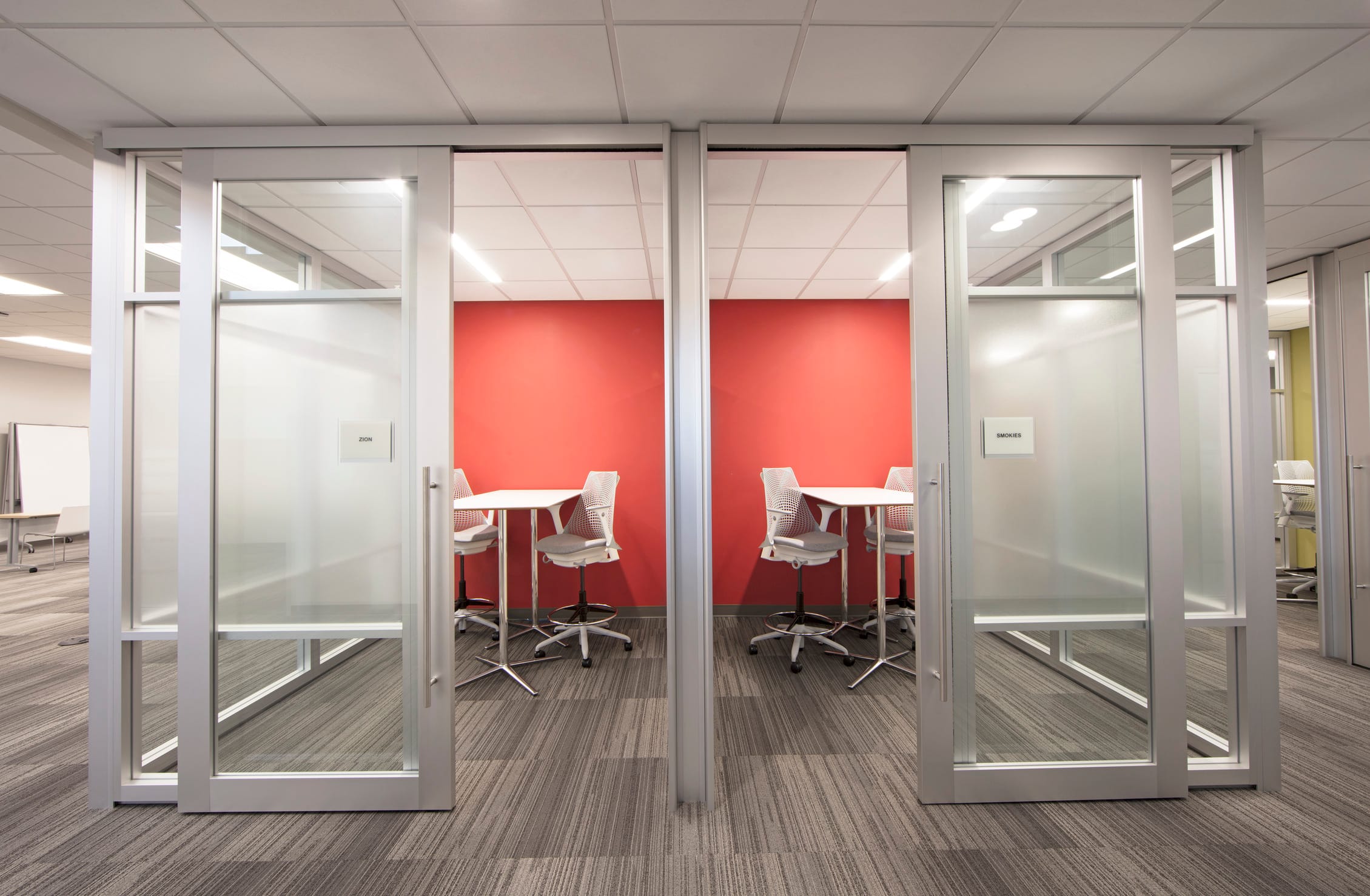 Designed with flexibility in mind, these glass-enclosed breakout rooms balance privacy and visibility—supporting both focused work and spontaneous collaboration. The use of frosted panels, warm red accent walls, and ergonomic furniture reflects BSA’s commitment to adaptive, people-centered workplace design.