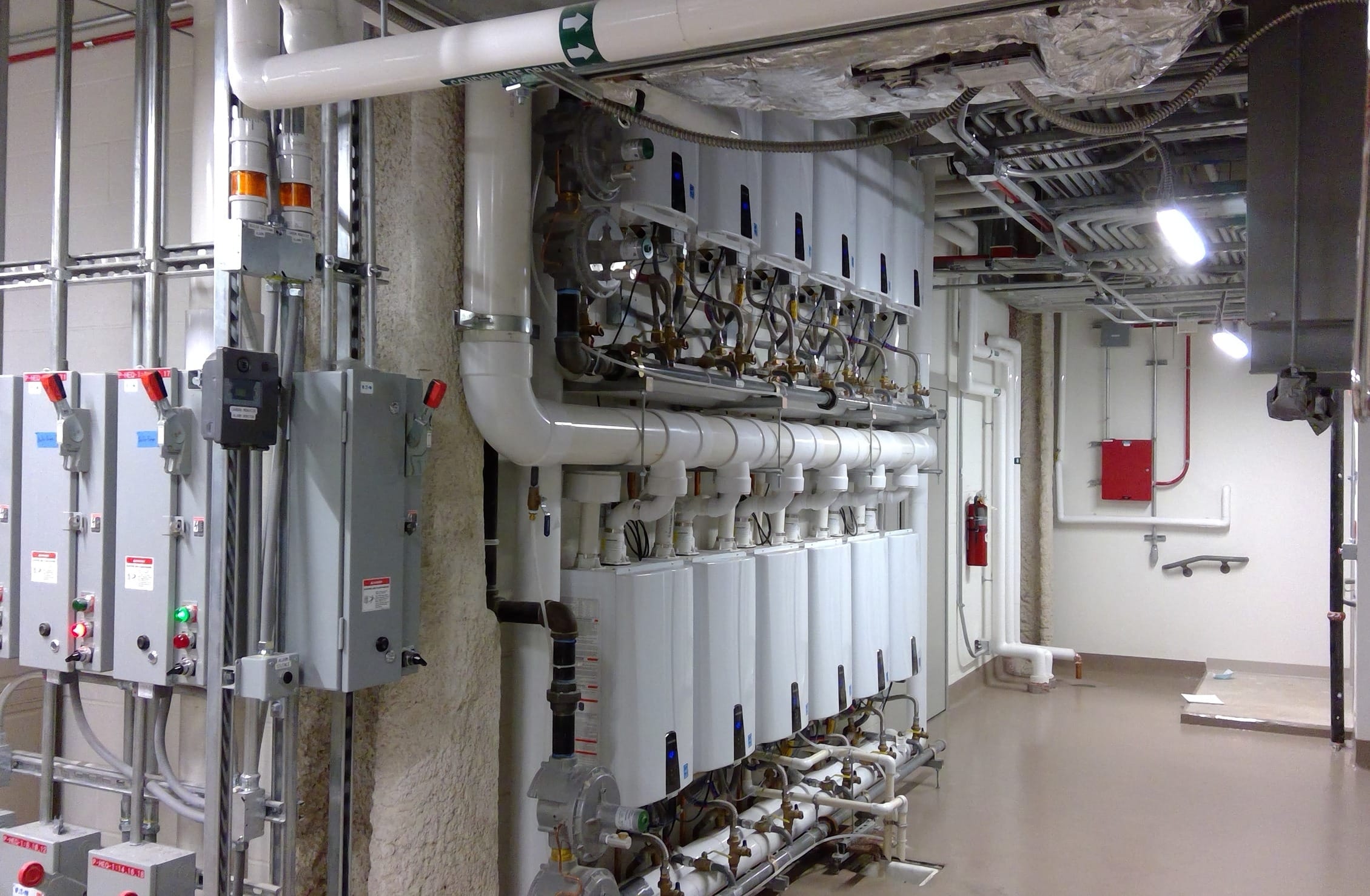 An industrial mechanical room filled with an array of white pipes, ducts, and metal conduits running along the ceiling and walls. Various pieces of equipment are strategically placed throughout the room. The space is a critical infrastructure system and shows BSA's expertise in MEP engineering.