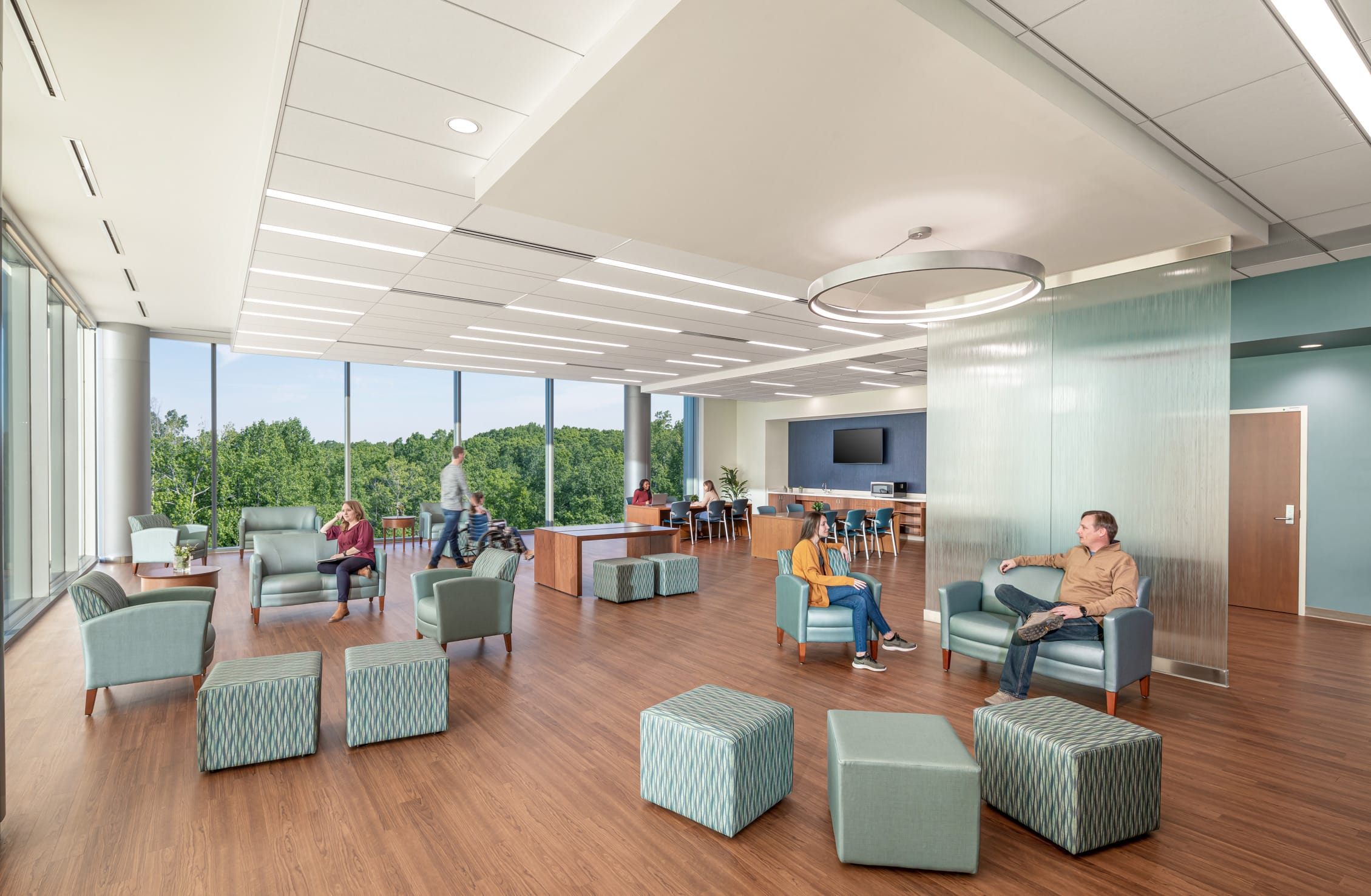 UNC Hospitals Hillsborough waiting room, featuring modern glass panels within the room to create separate spaces. Teal furniture is situated randomly through the spacious room. Floor-to-ceiling windows allow for ample natural lighting. This image showcases BSA's expertise in designing spaces that prioritize patient care.