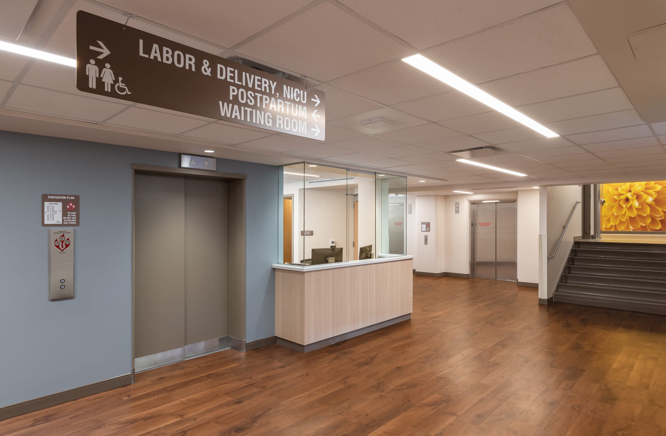 This image shows a reception or check-in area of the Cheyenne Regional Medical Center's maternal care department. A prominent brown directional sign hangs from the ceiling with symbols for men, women, and accessibility, indicating