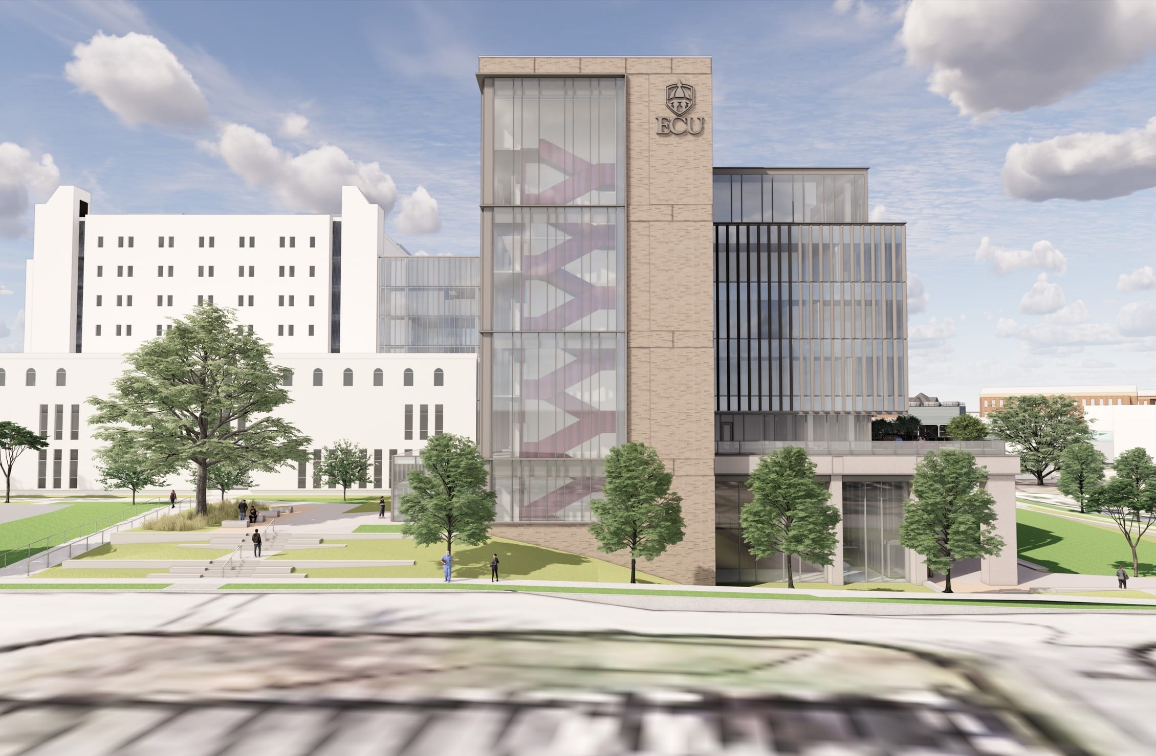 This rendering showcases another perspective of East Carolina University's campus development, featuring a striking academic building with distinctive architectural elements. The structure combines light brick with extensive glass facades, prominently displaying the ECU logo at the top of a dramatic glass stairwell tower that reveals purple interior elements. The building employs a stepped design with multiple levels and varying façade treatments, including vertical fins on the right portion. It connects to an existing larger white campus building visible on the left, suggesting this is an expansion or companion facility. The landscape design creates a welcoming approach with terraced green spaces, mature trees, and pedestrian pathways that guide visitors toward the entrance. The overall composition balances contemporary architectural expression with integration into the existing campus context while creating outdoor gathering spaces for the university community.