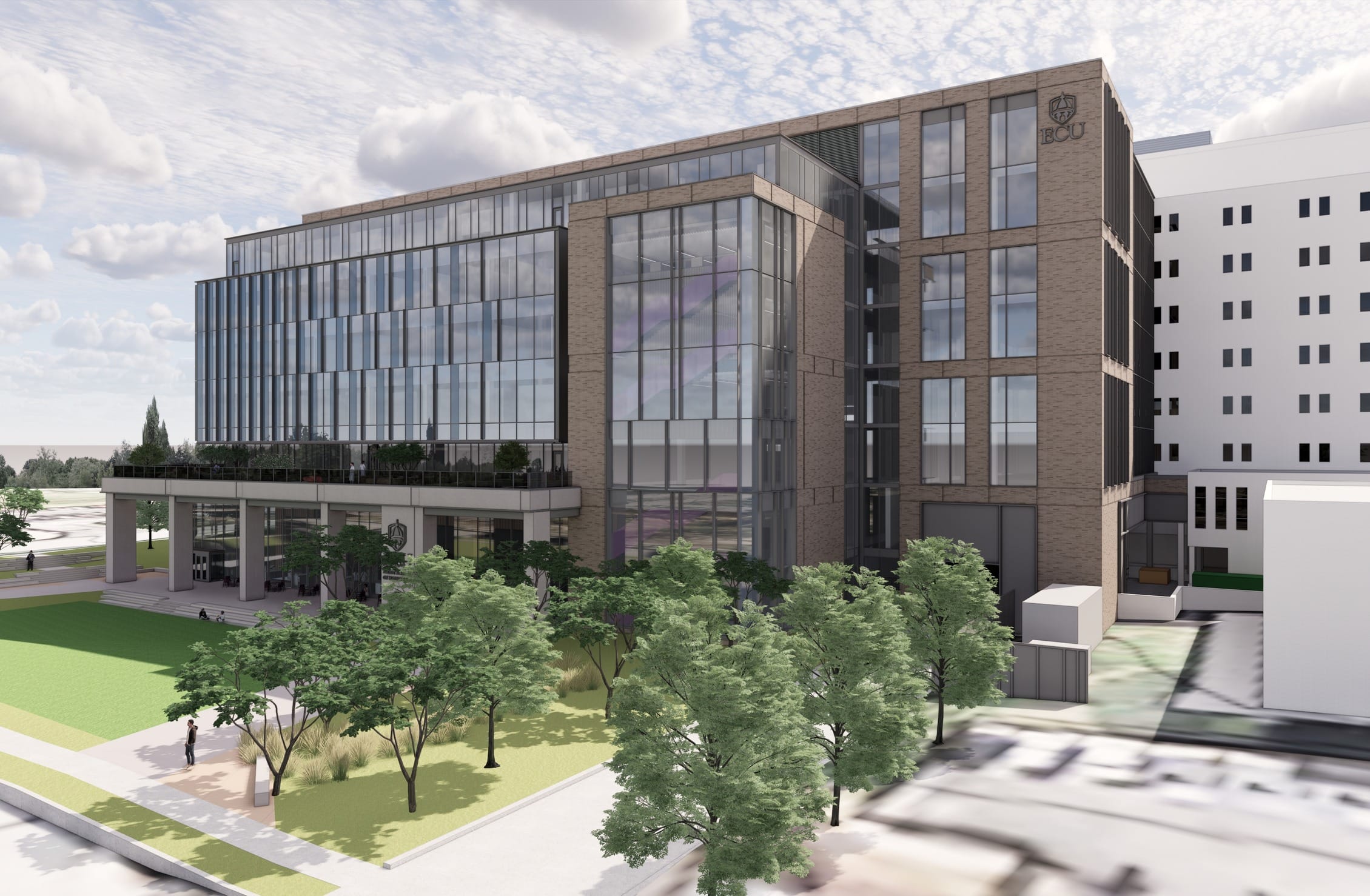 This rendering shows a modern academic building on East Carolina University's campus, as indicated by the ECU shield logo visible on the façade. The multi-story structure features a balanced design of brick cladding and extensive glass curtain walls, creating a blend of traditional campus materials with contemporary architectural elements. A dramatic glass atrium corner provides vertical connectivity and natural light penetration. The building's podium level includes a covered entrance area with columns, creating a welcoming approach. Surrounding the building is thoughtfully landscaped green space with mature trees, pedestrian pathways, and gathering areas that integrate the structure into the campus environment. Adjacent buildings suggest this is part of a larger medical or academic complex, likely housing classrooms, research spaces, or administrative offices for the university.